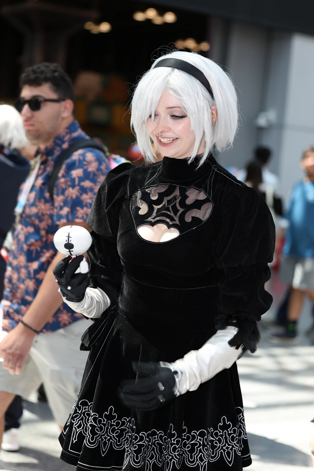 A white-haired cosplayer in a black lace costume holding a small plush figure