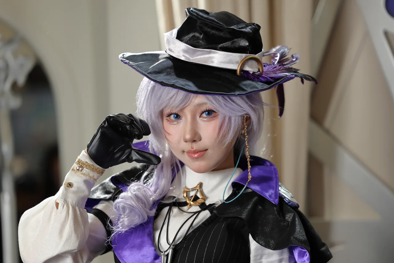 A cosplayer with lavender hair, a black hat and a purple cape looking toward the camera
