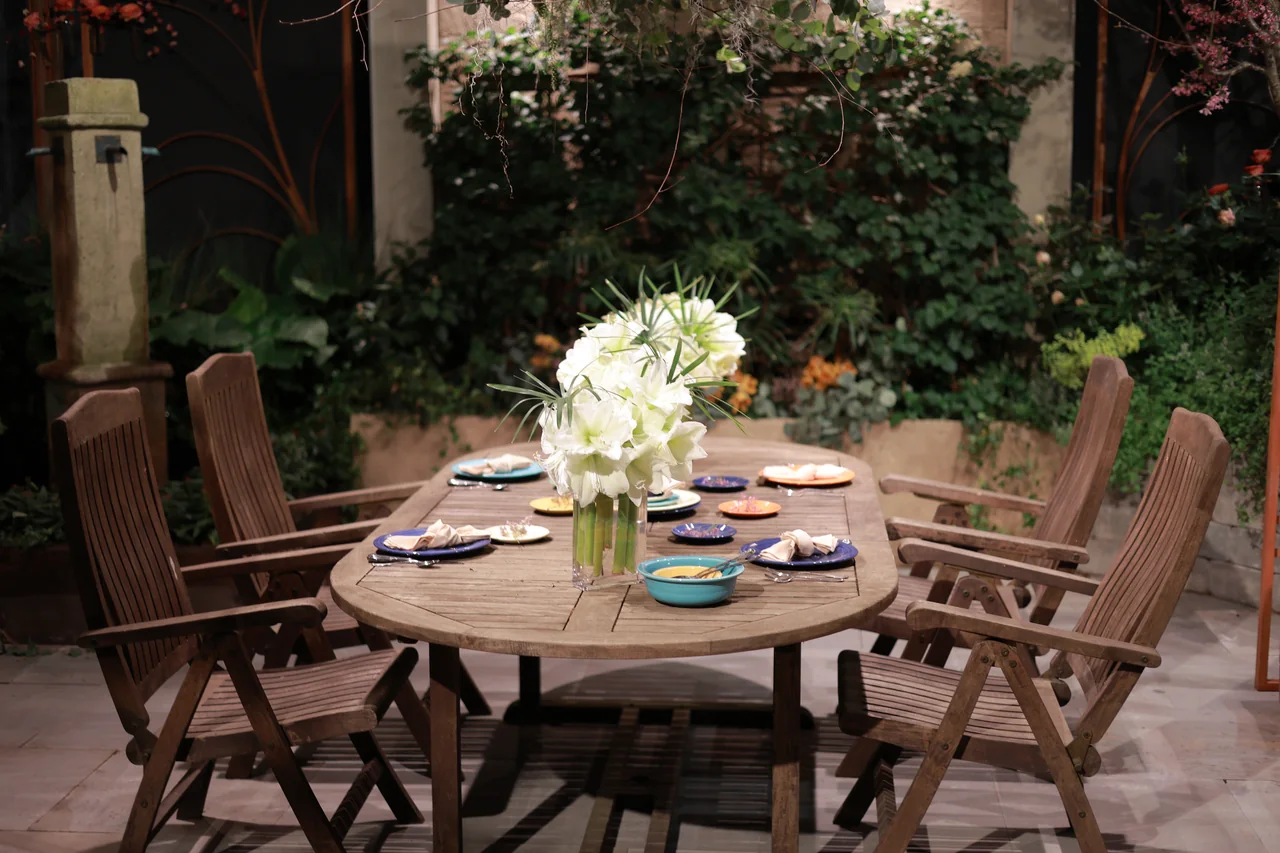 A wooden garden dining table set with dishes and a vase of white flowers