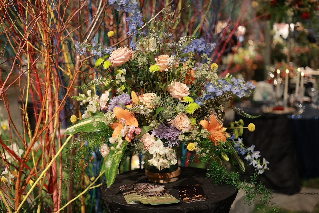 An abundant arrangement of peach roses, blue flowers and delicate branches in a dark garden display