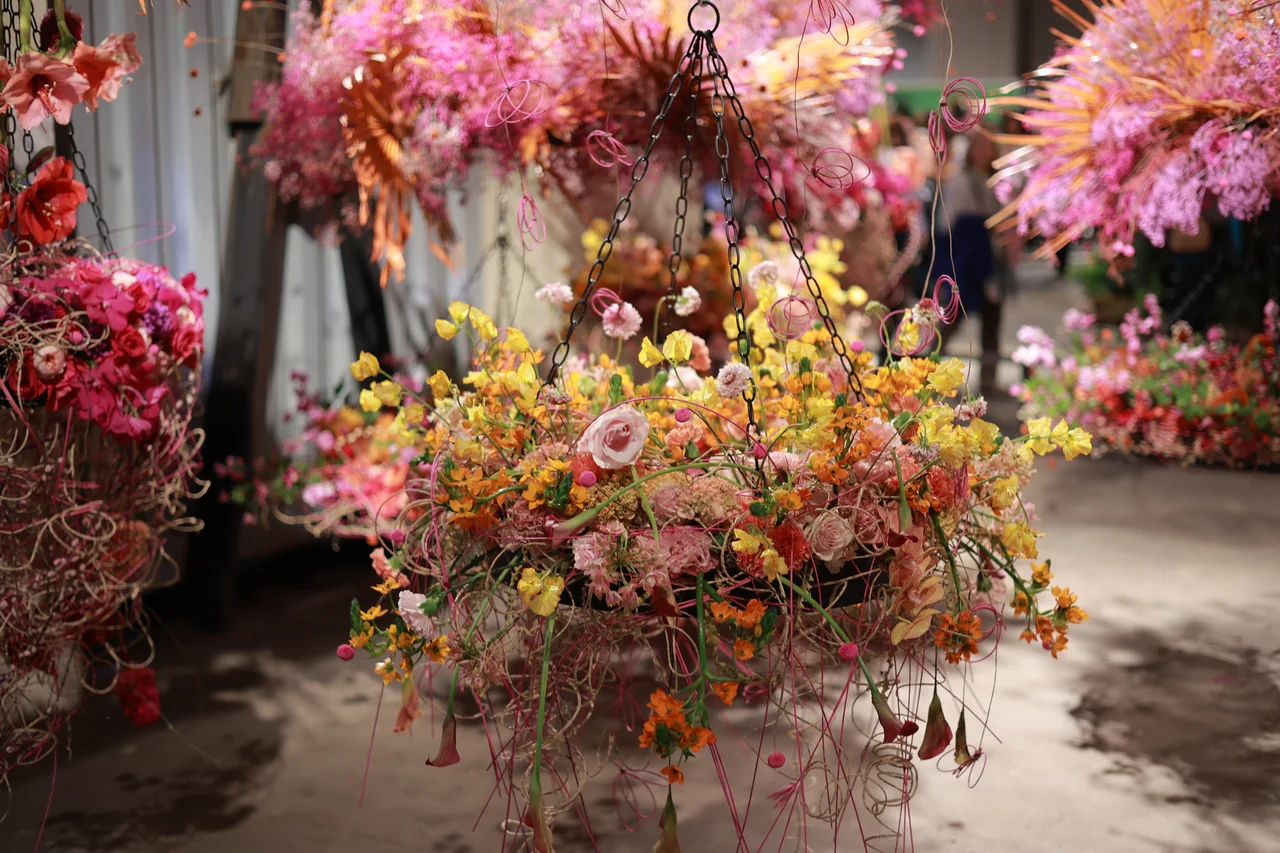 A hanging arrangement of pink roses and small yellow and orange flowers, surrounded by suspended floral sculptures