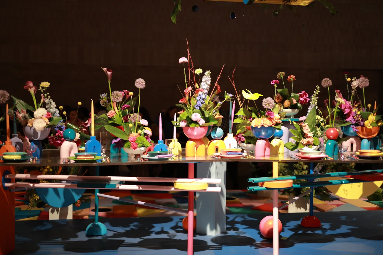 A long display table lined with flowers in brightly colored vases under spotlights