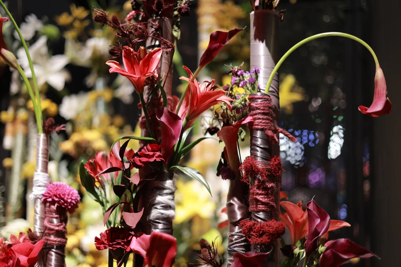 Red lilies and a single curved calla lily stem among ribbon-wrapped vertical poles