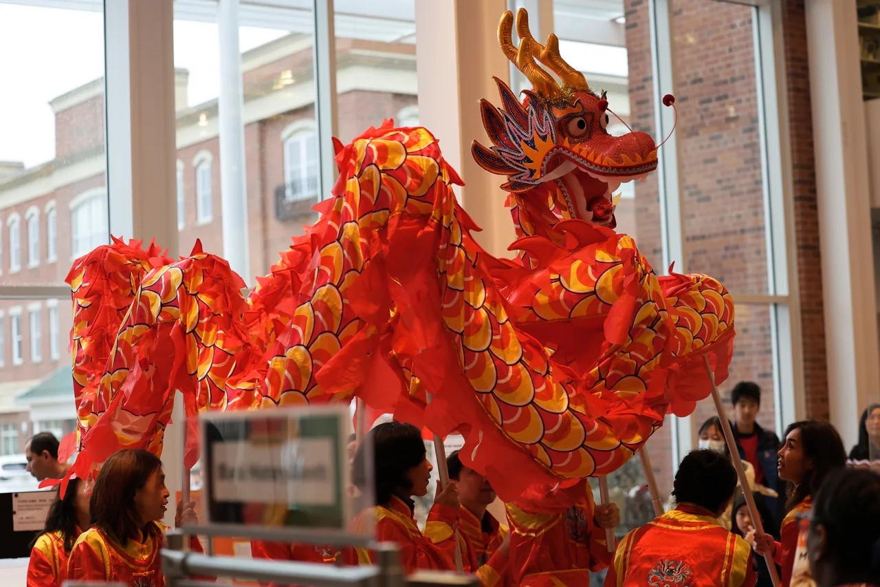 A red and gold dragon weaving through a Lunar New Year gathering in a library