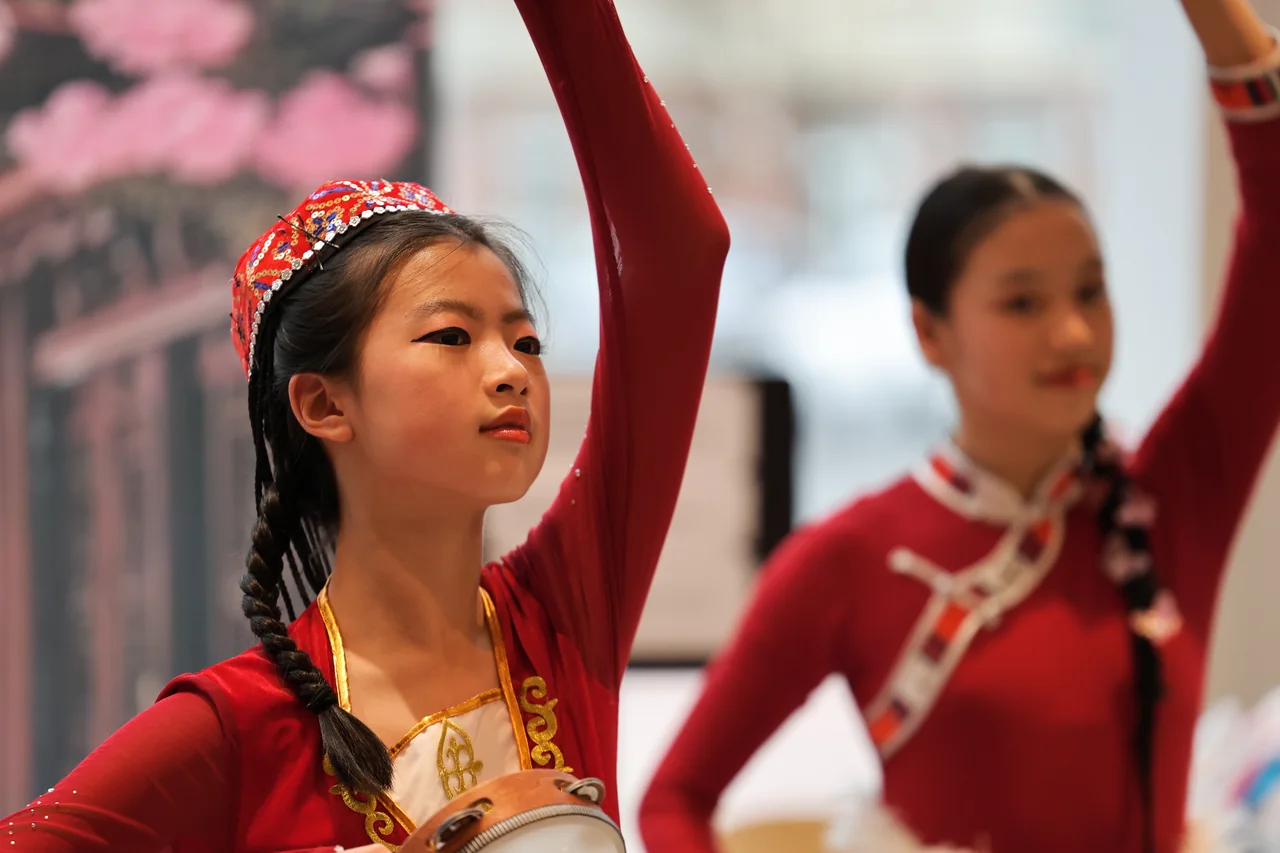 A dancer in red raising her arm in front of another performer