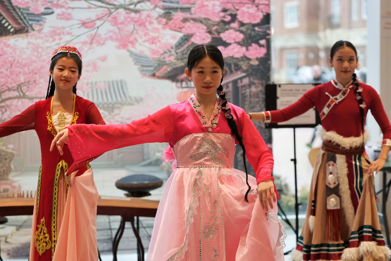 Three dancers in pink and red performing with arms extended