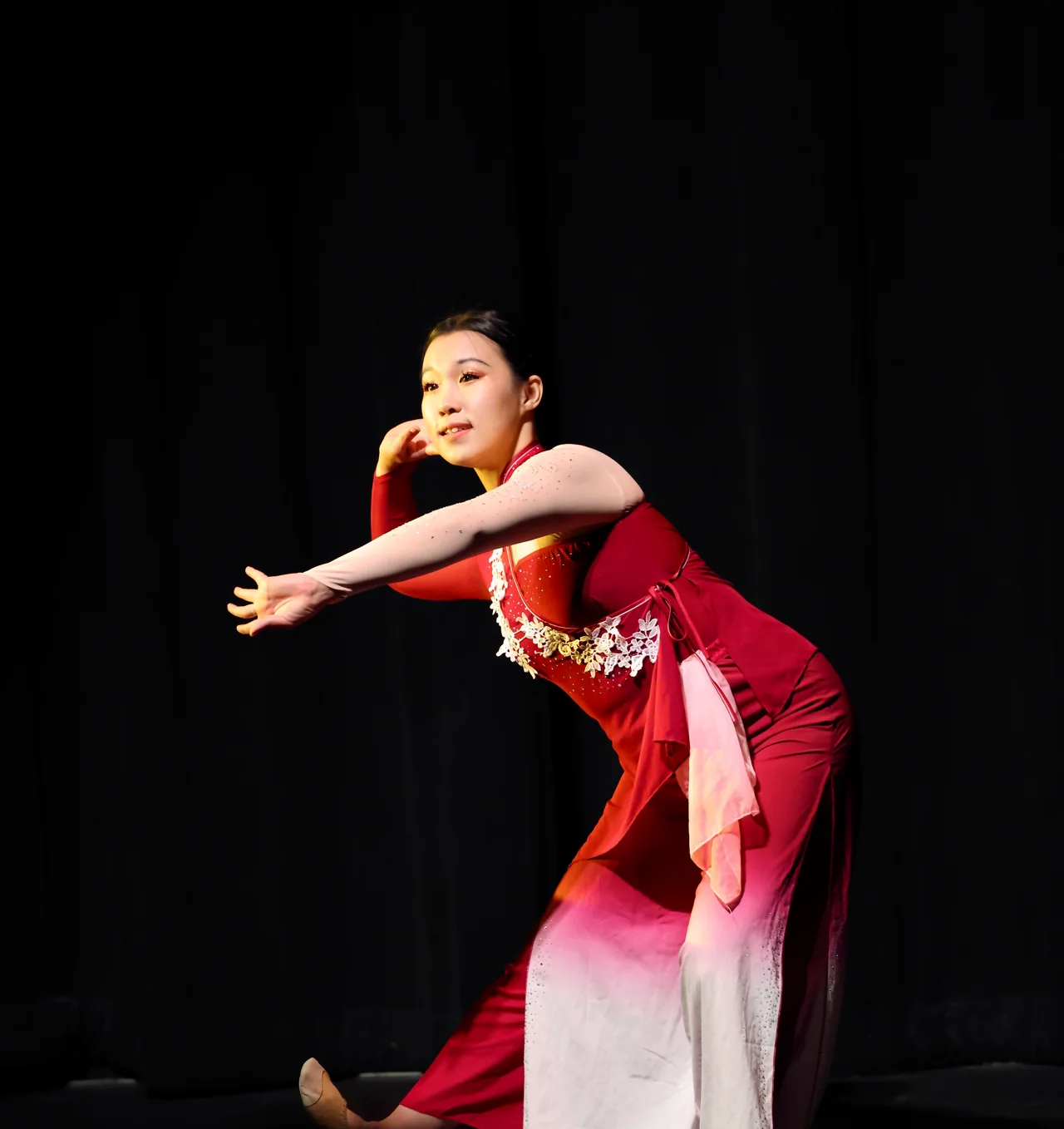 A dancer in red reaching across the stage against a dark curtain
