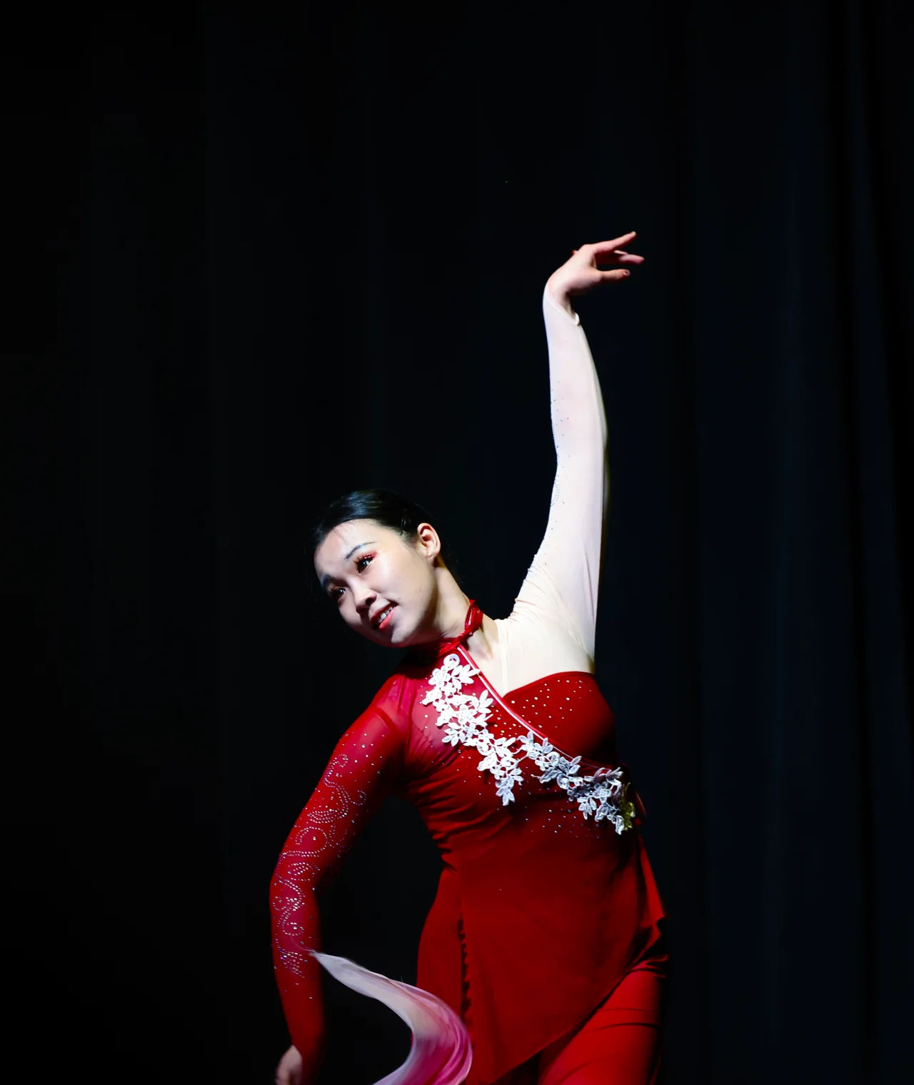A dancer in a red dress extending one arm above her head on a dark stage