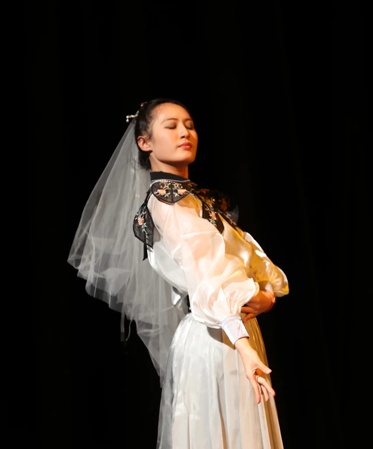 A performer in a white veil standing in a pool of stage light
