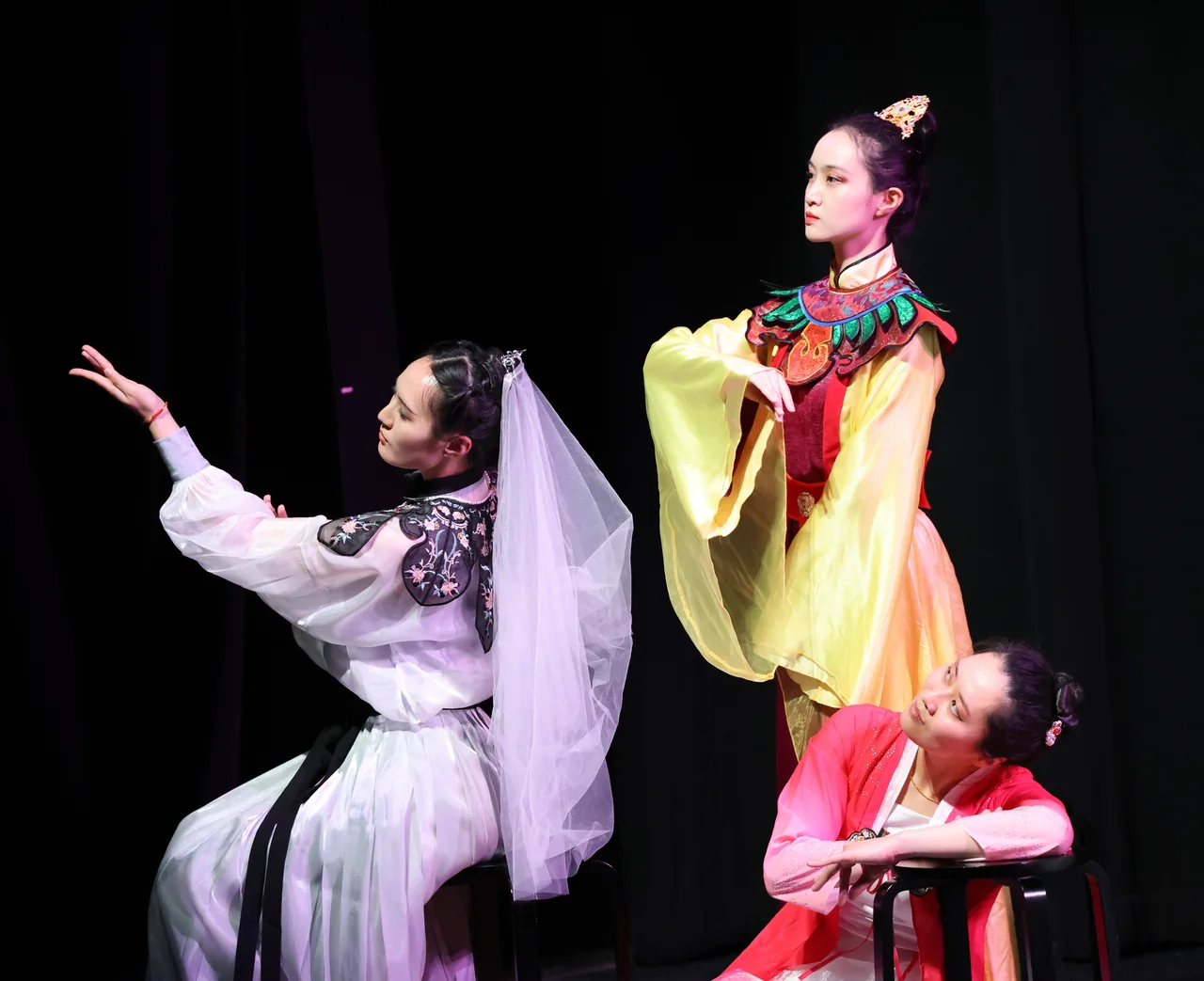 Three performers in pastel costumes forming a layered tableau