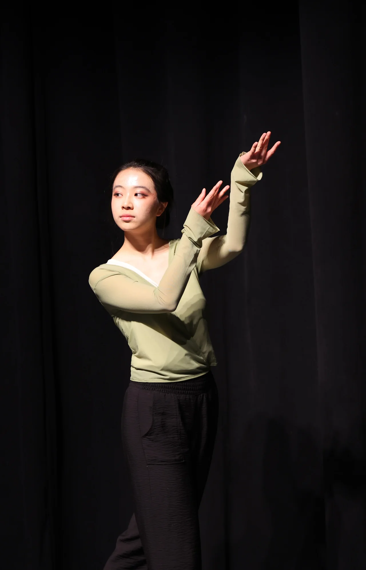 A solo performer in a green top lifting her hand into the stage light